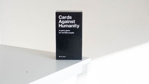 Card against humanity game box sitting on the edge of a white table.