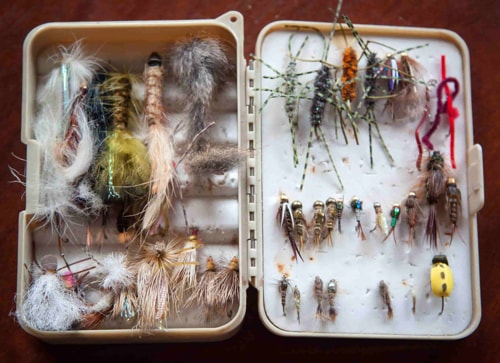Old fashioned tackle box full and messy with different kinds of insect fishing lures.