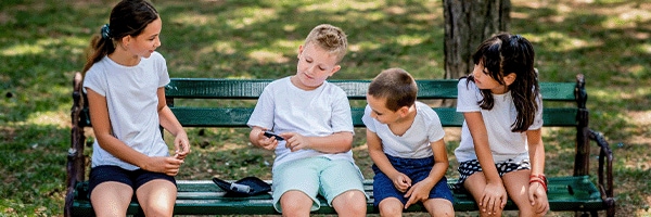 Child checking blood sugar on park bench while friends watch