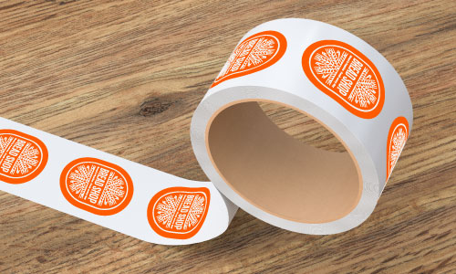 custom oval paper roll label roll with orange and white bread bakery logo printed on them unrolling on a wood surface