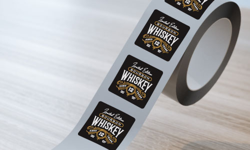 custom square paper roll label roll with whiskey logo on a wooden surface