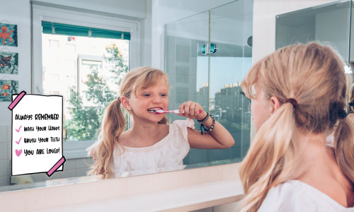 Child standing in front of a mirror brushing her teeth and there is a sticker on the mirror